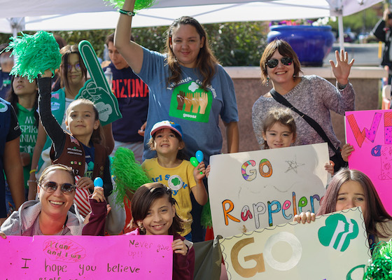 volunteers and girl scouts holding up colorful signs encouraging participants at over the edge
