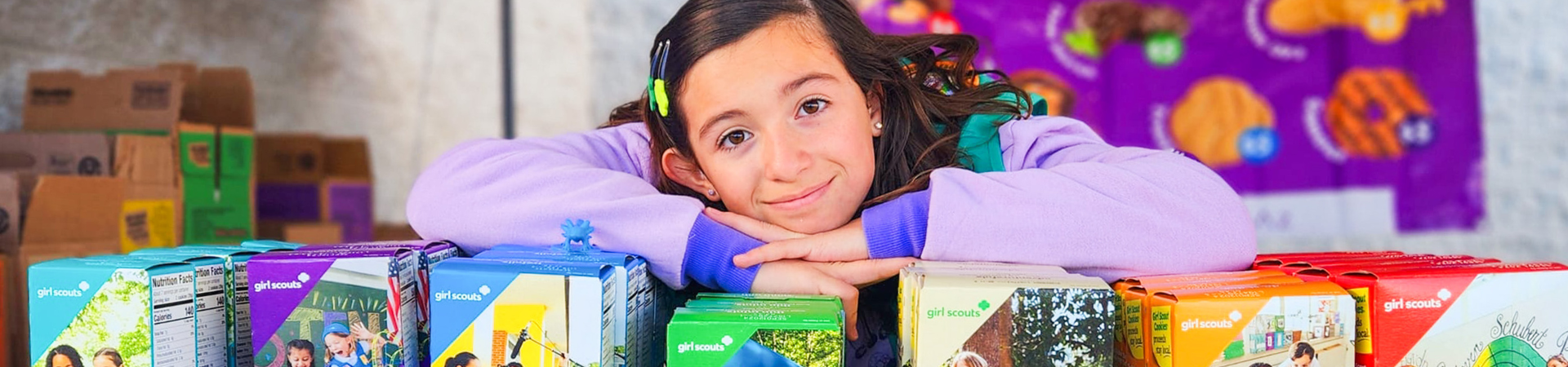  girl scout wearing uniform sash putting trefoil girl scout cookie boxes into cookie transport bag 