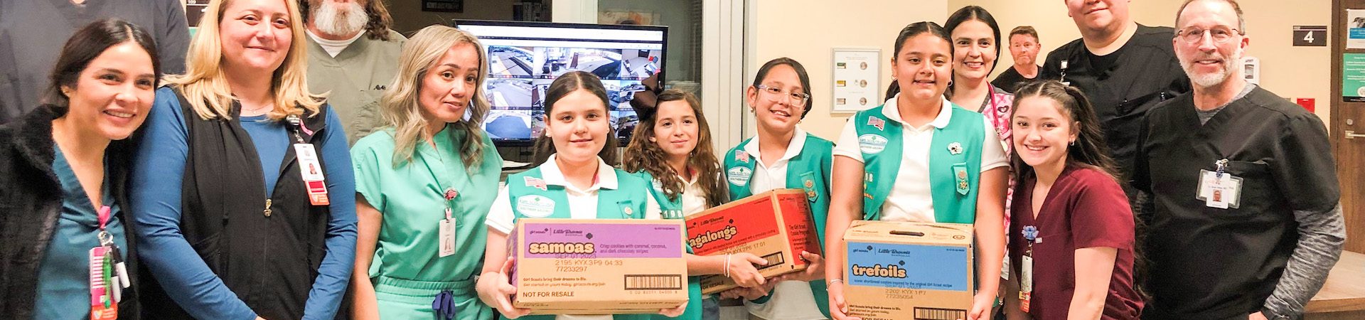  large group of girl scouts from every level posting with labeled cookies for heroes boxes 