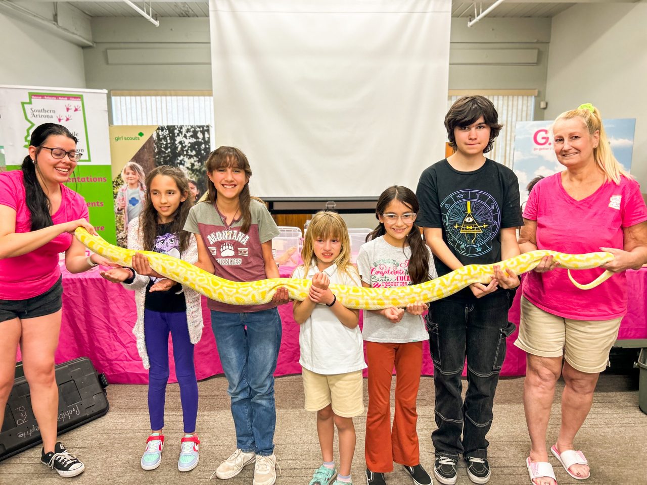 community partners and girl scouts hold up large snake