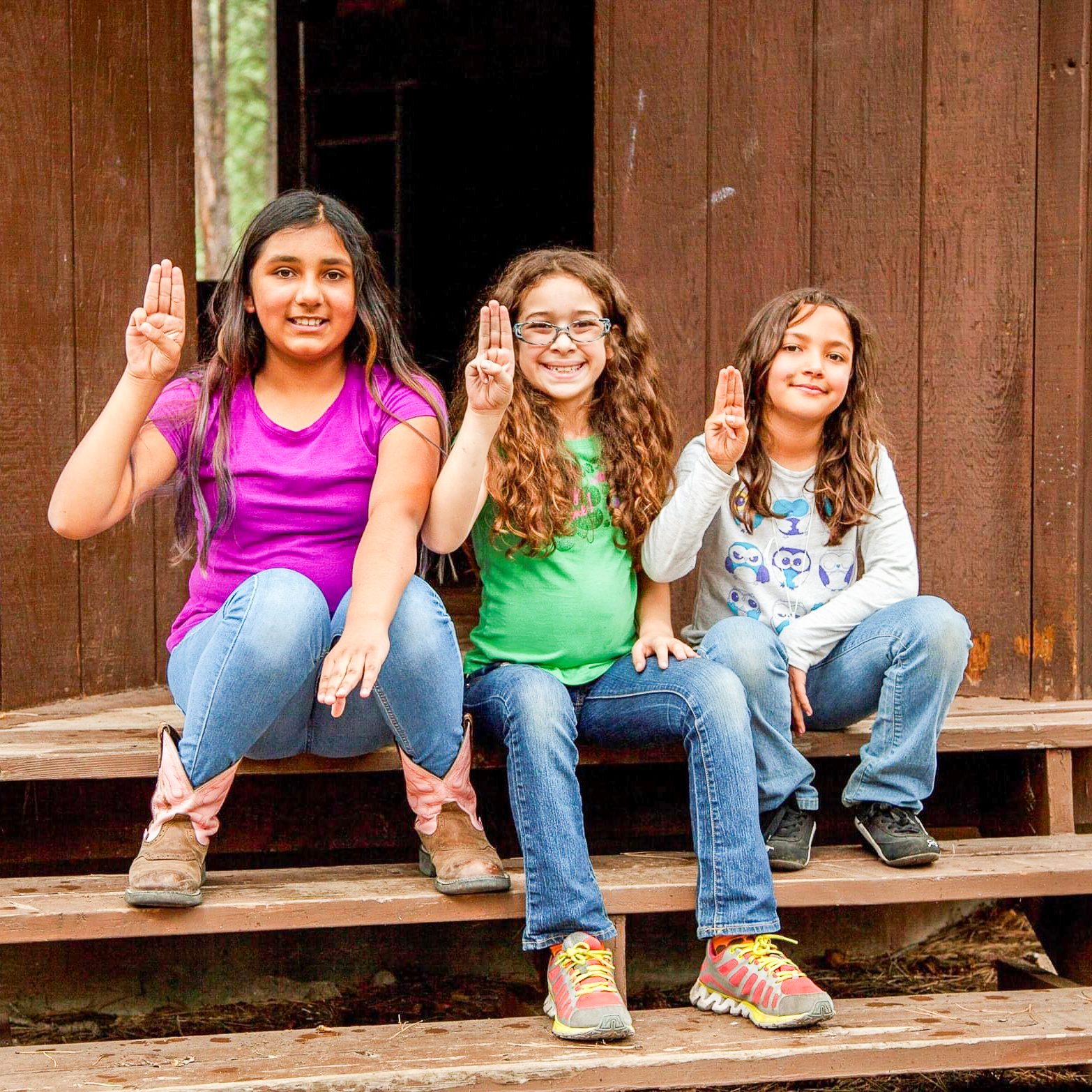 three girl scouts sitting and holding up the girl scout hand sign