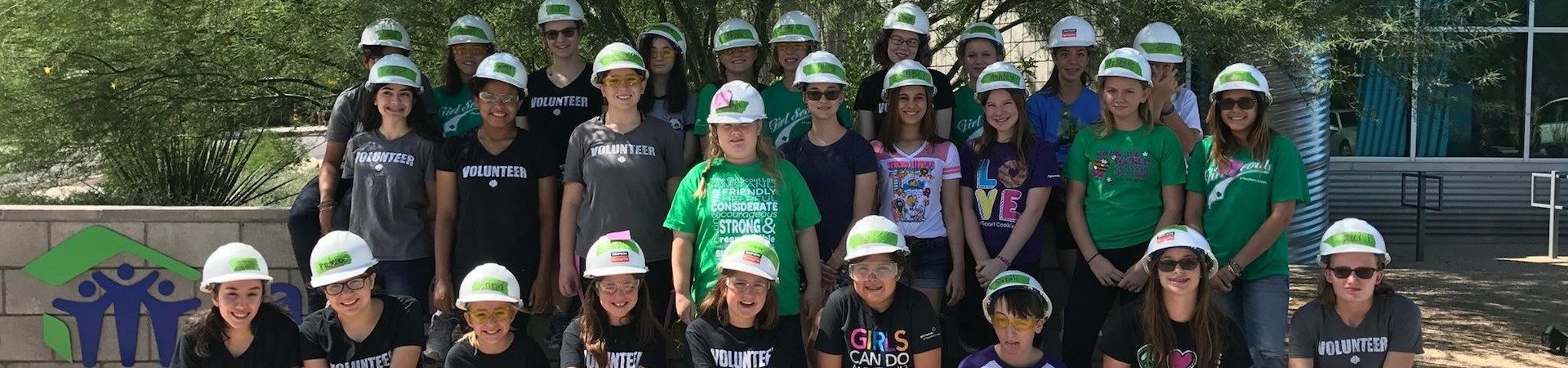  girl scout volunteer corps standing in front of habitat for humanity with hard hats 